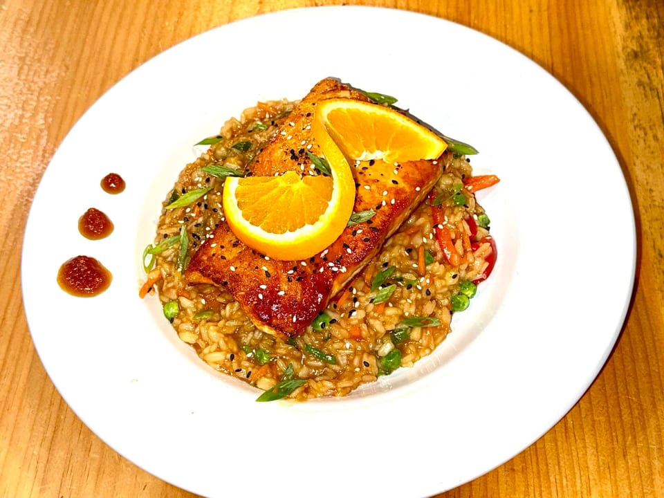 Pan-seared salmon with sesame seeds and orange slices, served over risotto with vegetables.