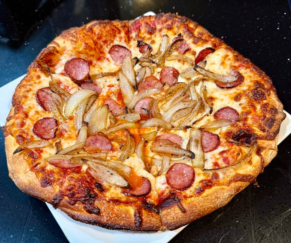 A whole pizza with sausage and caramelized onions on a white plate, on a dark countertop.